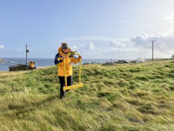 Person in a yellow jacket using survey equipment in a rural location
