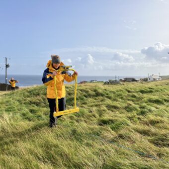 Person in a yellow jacket using survey equipment in a rural location