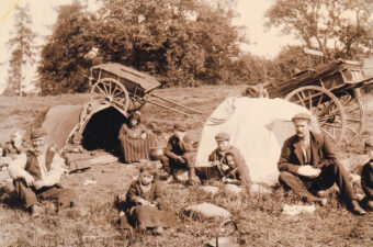 Black and white photo of a Gypsy/Traveller family in a field with their wagons
