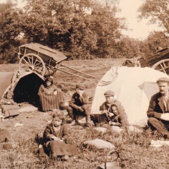 Black and white photo of a Gypsy/Traveller family in a field with their wagons
