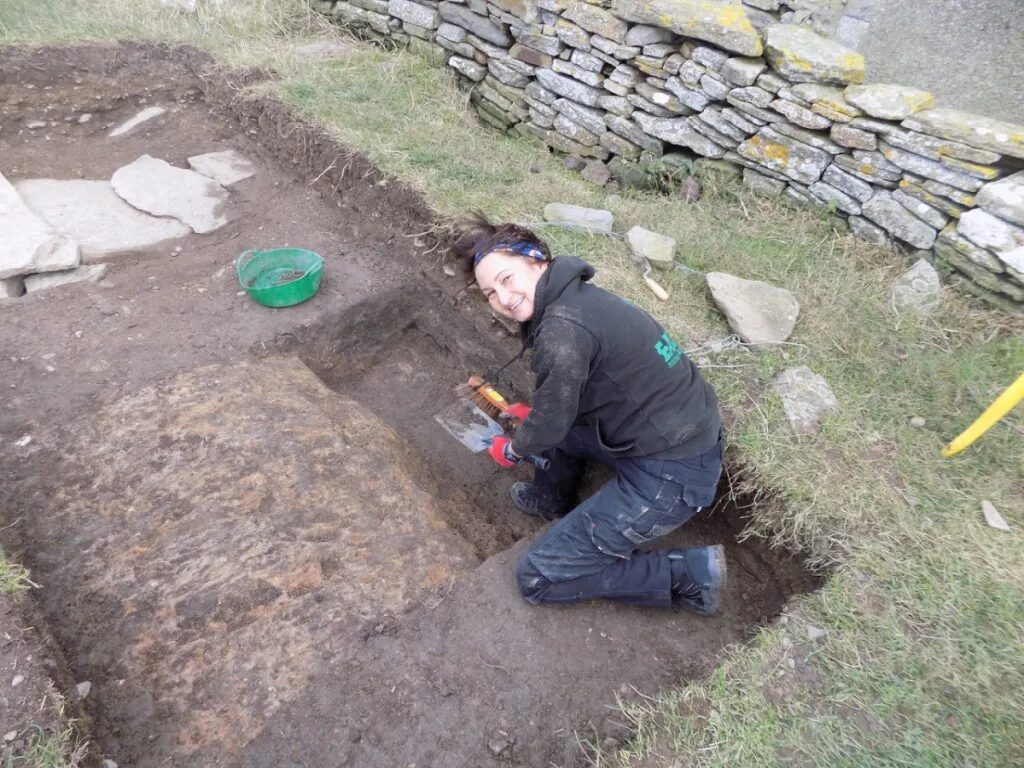 Person in an archaeological trench smiling at the camera