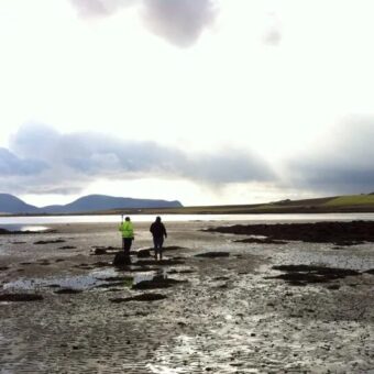 Two people walking over a beach at low tide