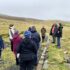 People standing outdoors at an archaeological site listening to someone speak