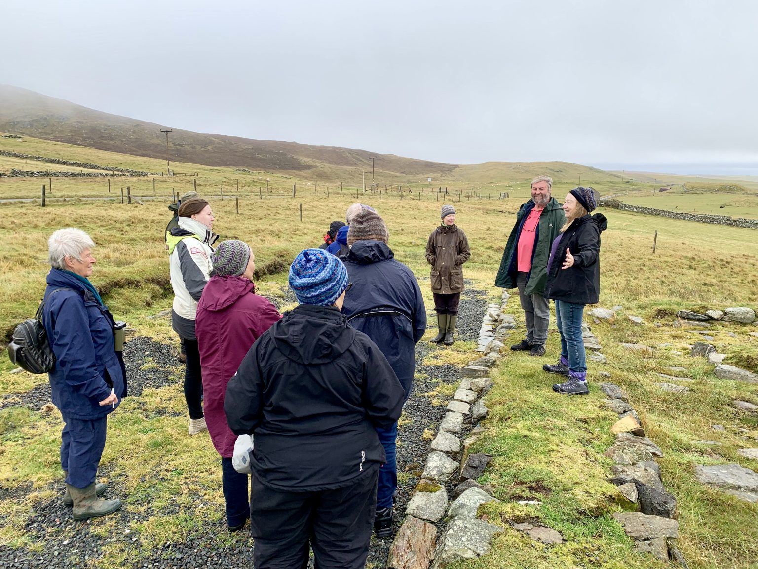 People standing outdoors at an archaeological site listening to someone speak