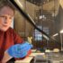 Photo of a woman in a red jumper wearing blue disposable gloves and holding a small carved stone object in a museum
