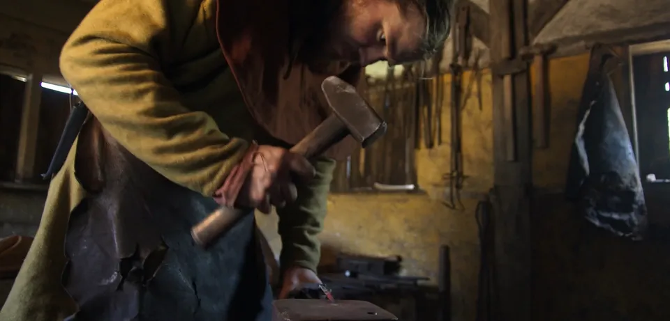 Photo of a man in medieval clothing using a hammer in a forge